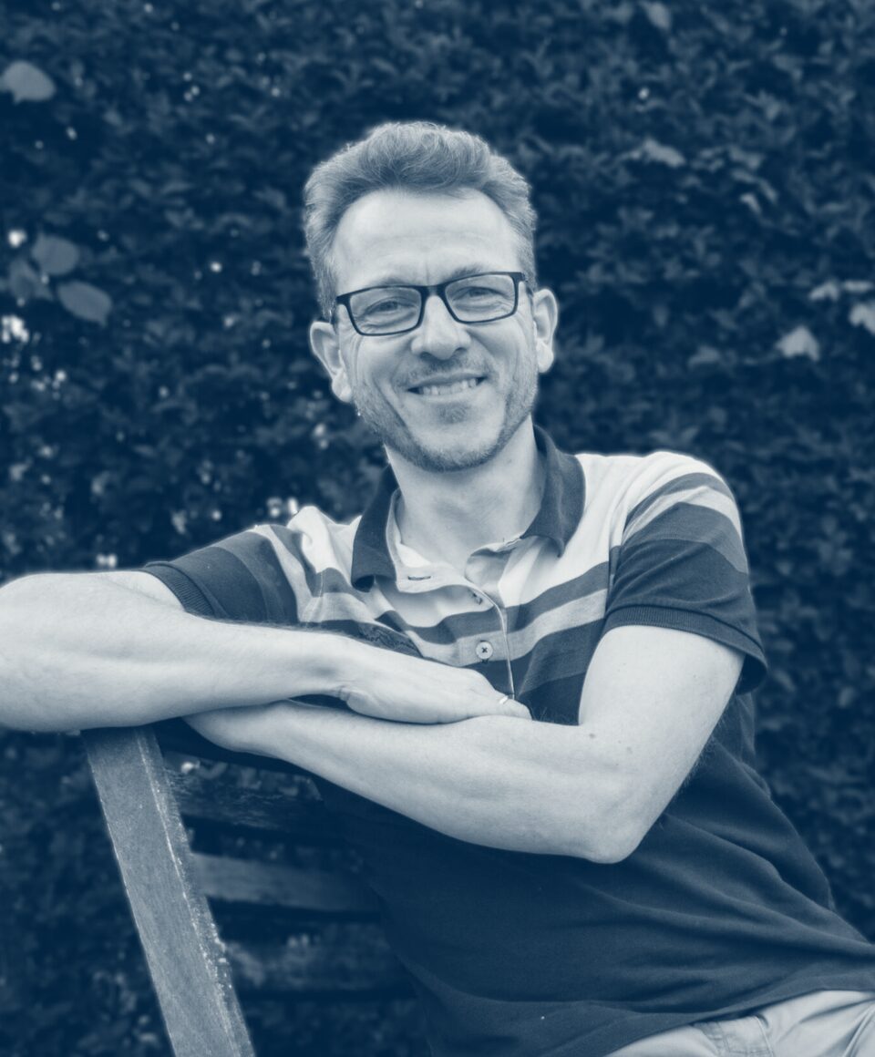 Pierre-Henri Delaval, souriant, appuyé sur le dossier d'un banc de jardin.
